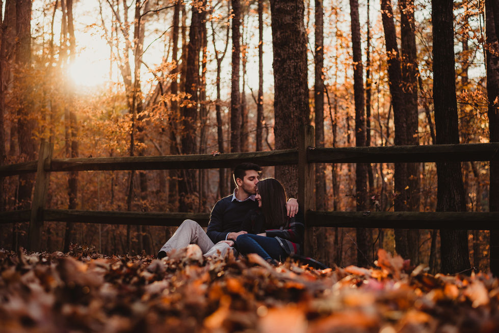 Couple sitting in autumn forest near wooden fence.
