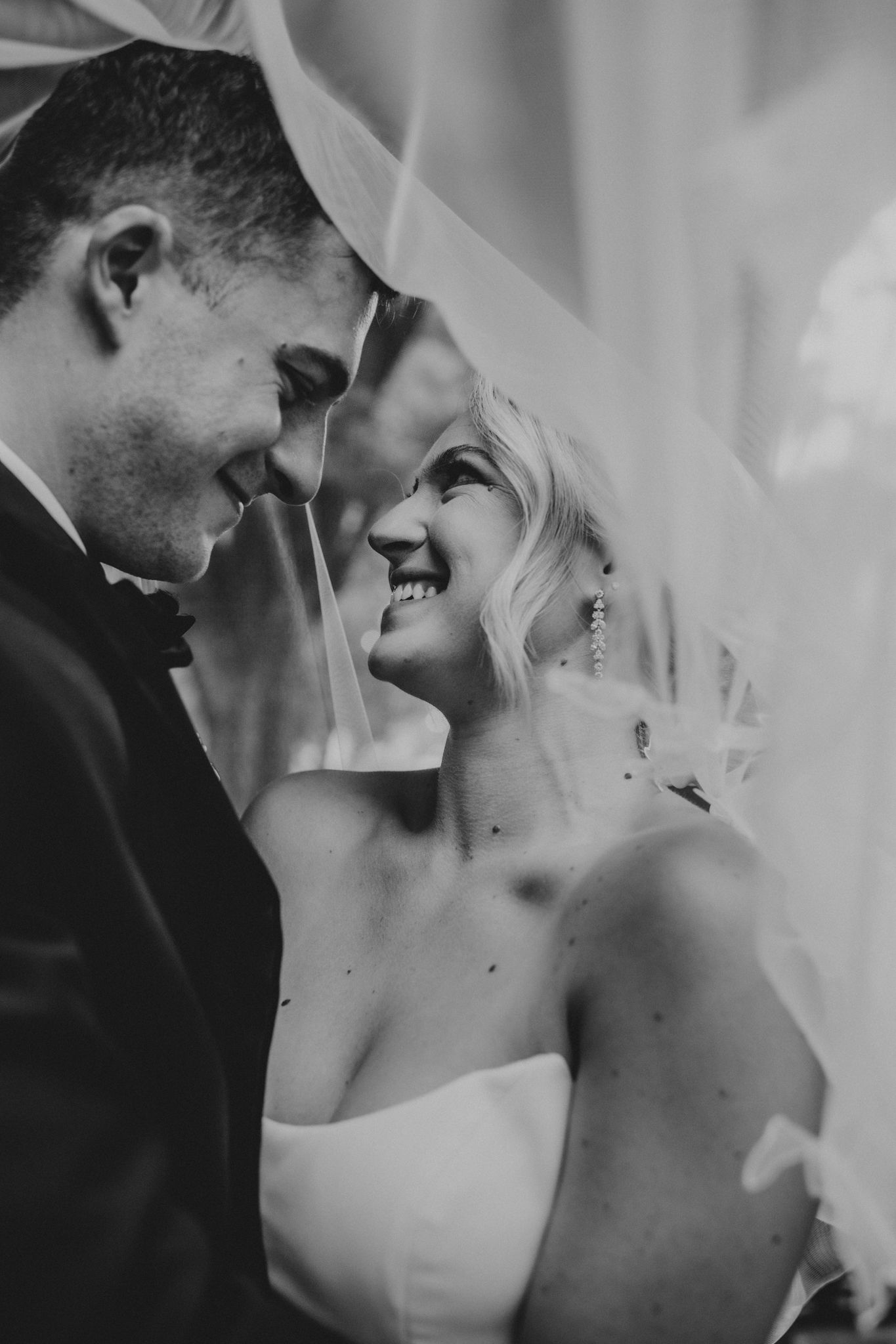 a black and white portrait of the bride and groom under the bride's veil