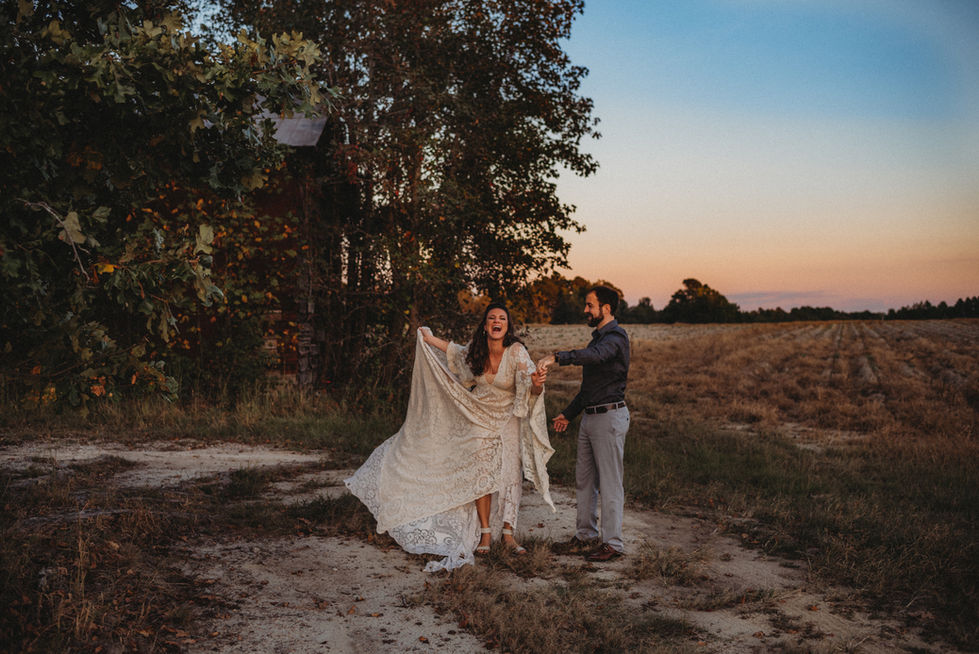 a couple dancing alone at the edge of the woods in front of a field on their wedding day