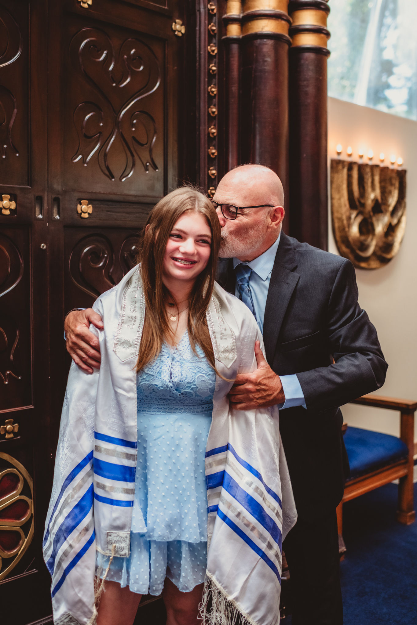 Man kisses girl's head at a special bat mitzvah ceremony.