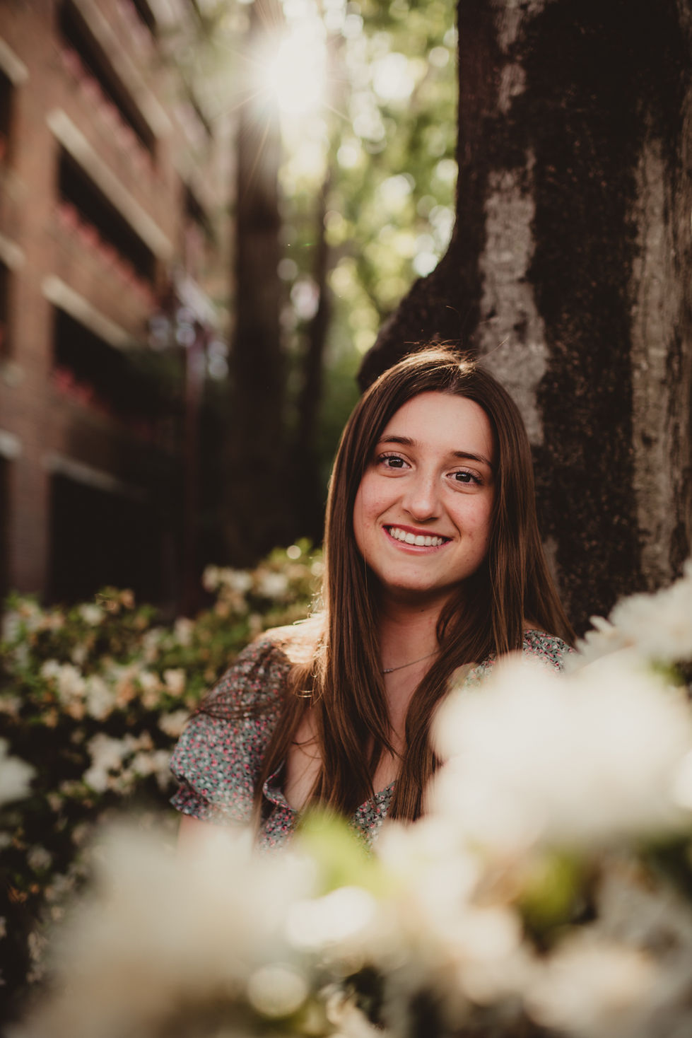 Smiling person outdoors with flowers and trees.