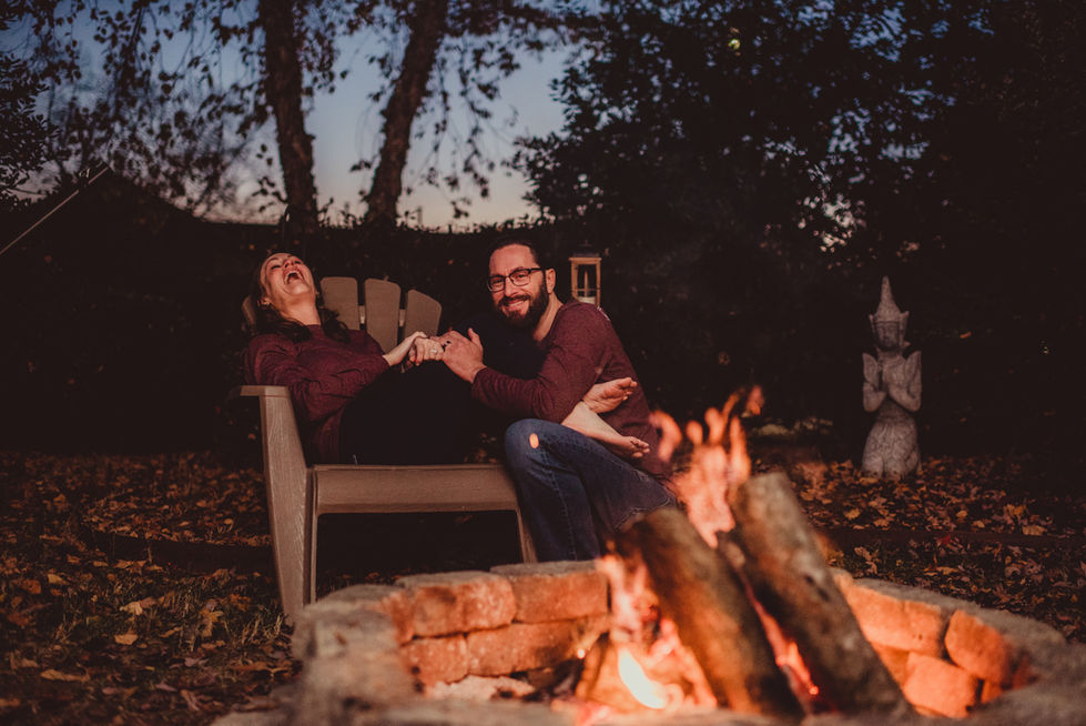 Couple laughing by a cozy outdoor fire pit.