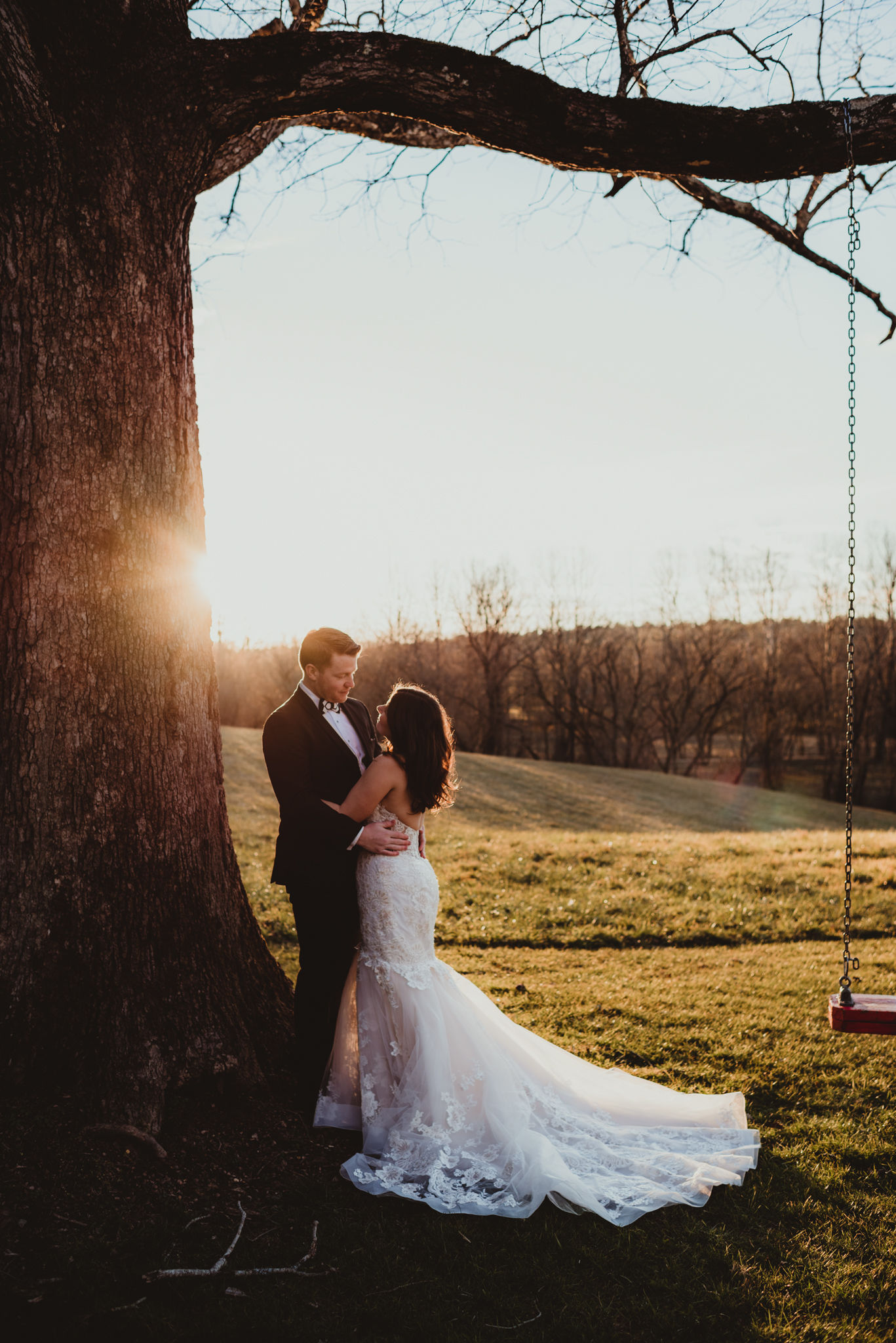 a portrait of a bride and groom near a tree with a swing and the glowing sunset in the background