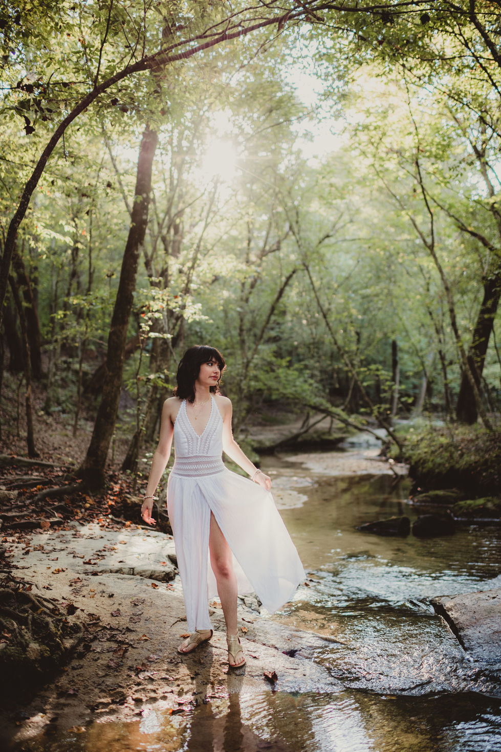 Woman in white dress standing in a forest stream.