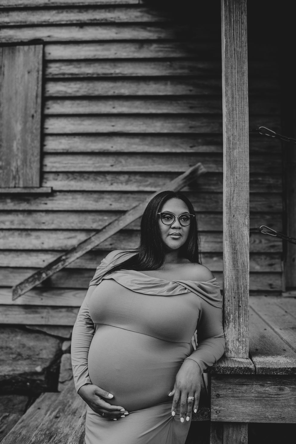 Woman in glasses poses by rustic wooden building.
