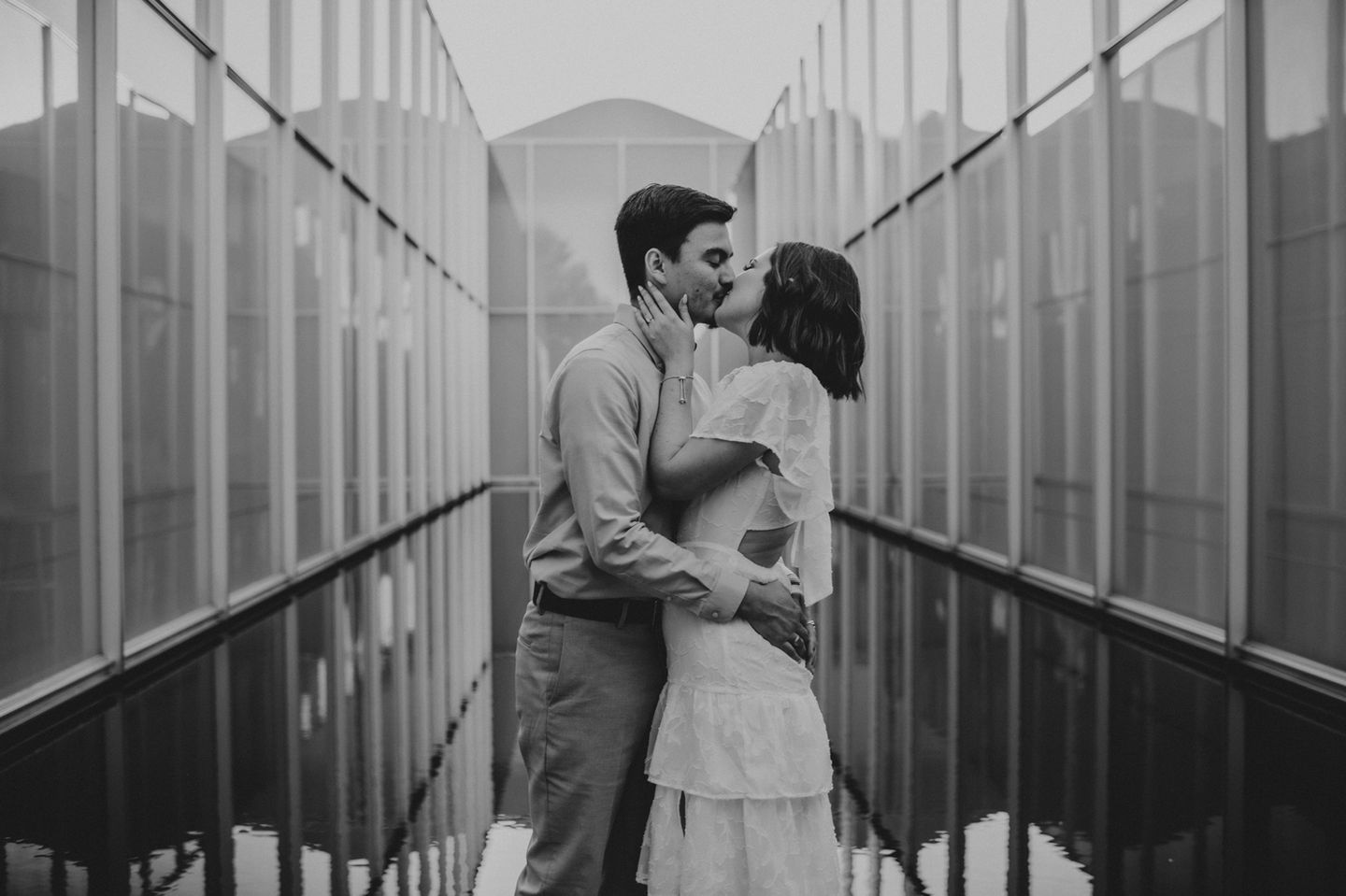 Couple kissing between reflective glass walls, black and white.