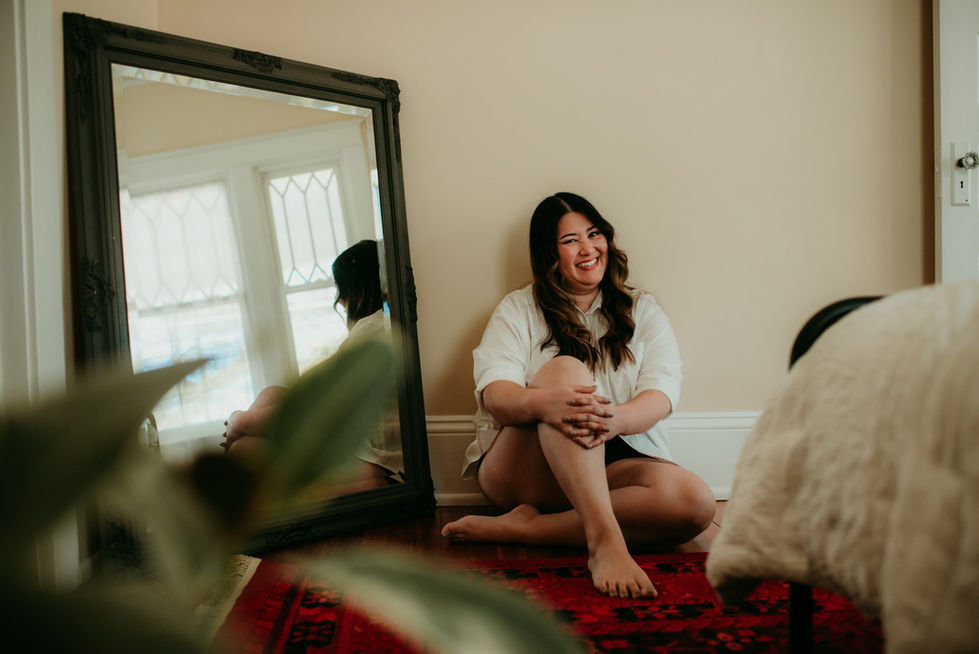 Woman sitting on floor, smiling near a mirror.