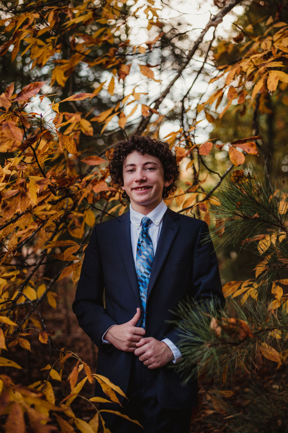 Young person in suit, surrounded by autumn leaves, for Mitzvah portraits.