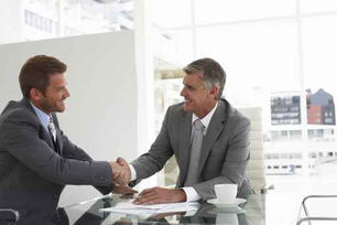 Zwei Männer in Businessanzügen, welche sich die Hand geben und zufriedene Gesichter haben.