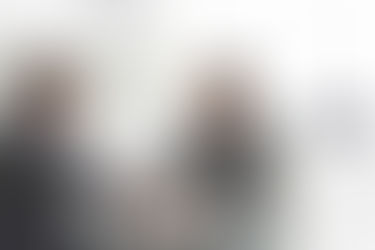 Zwei Männer in Businessanzügen, welche sich die Hand geben und zufriedene Gesichter haben.