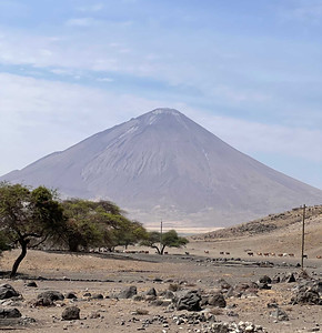 A thumbnail image, featuring a distant view of Ol Doinyo Lengai, with a dry and rocky valley and some lonely trees, in the foreground.