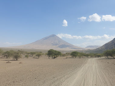 A thumbnail image, featuring a distant view of Ol Doinyo Lengai, with a dry and rocky valley and some lonely trees, in the foreground.