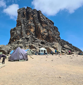 A thumbnail image, featuring a campsite with several tents, in front of a lonely rock wall.