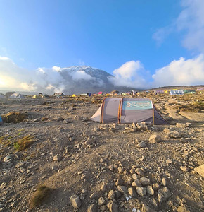 A thumbnail image, featuring a single tent in the foreground, displaying a green flag featuring the yellow Stunning Kilimanjaro logo, standing out against the rugged landscape, with a campsite in the background.