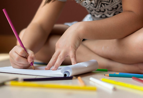 Picture of a child using colored pencils to color a page kneeling on the ground.