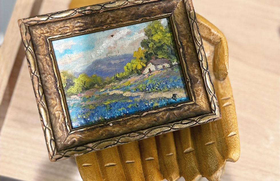 Picture of a small painting in a hand shaped wooden holder.