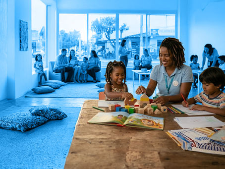 Foto de uma sala com crianças e pais sentadas no fundo, com um filtro azul sobre a imagem. Sobreposta, foto colorida mostra uma educadora negra e duas crianças, uma negra e uma com aparência indígena, sentados em volta de uma mesa para brincar.