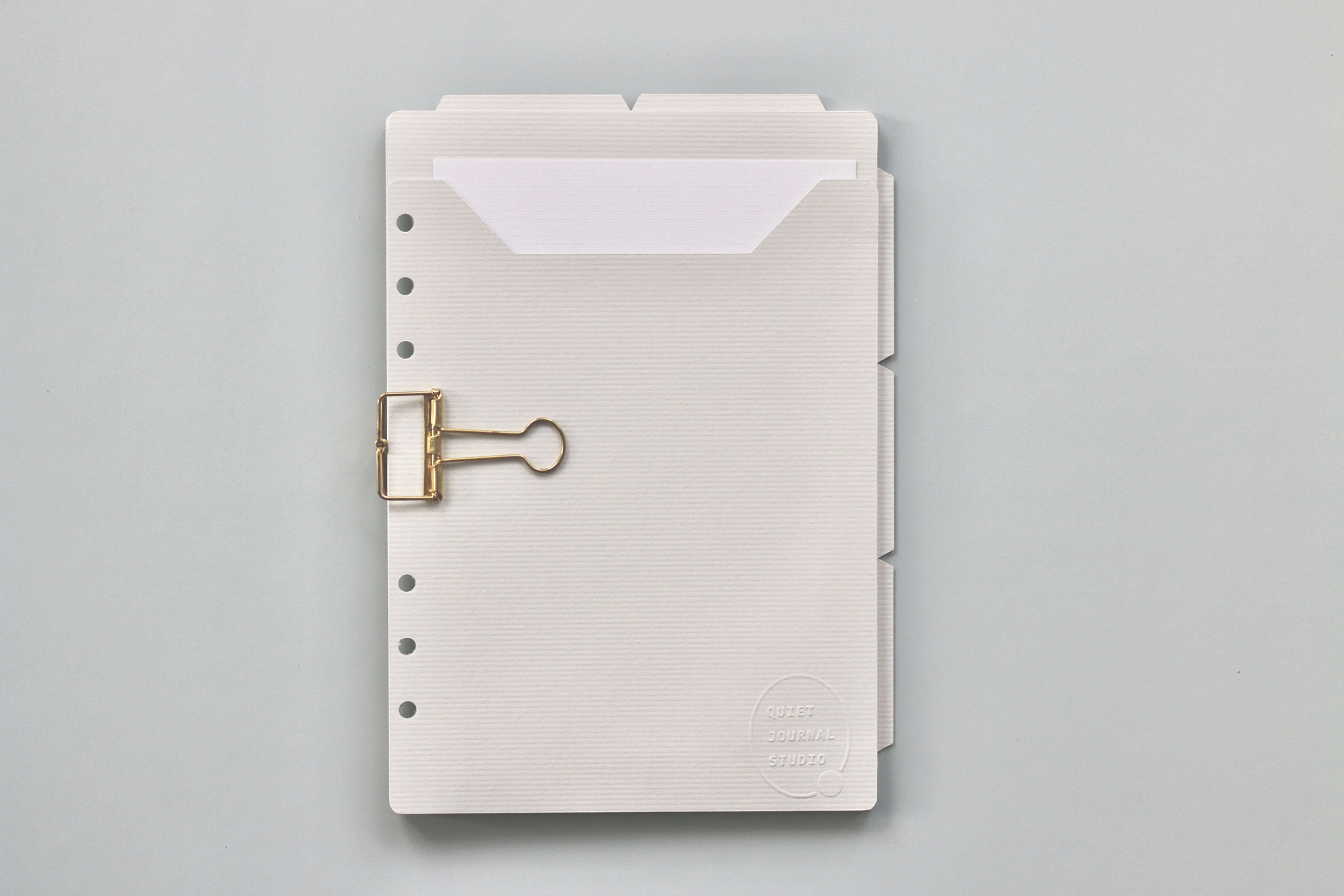 Gray divider with pocket and  white paper, and gold clip, on a gray background.