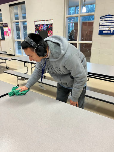 Jeremy cleans a table with a cloth.