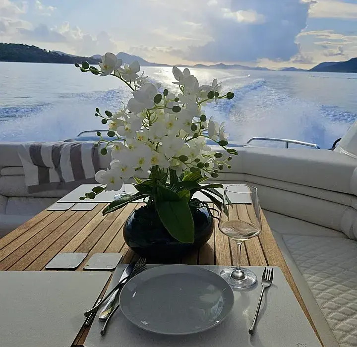 Gedeckter Esstisch auf dem Deck einer Yacht mit Blumenarrangement und Meerblick bei Sonnenuntergang – romantische Atmosphäre an Bord.