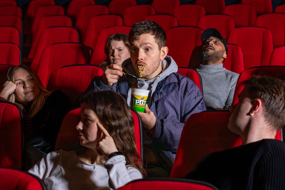 A man slurping a pot noodle in the cinema and people sat near him looking unimpressed, photographed by London PR photographer Harvey Aspell