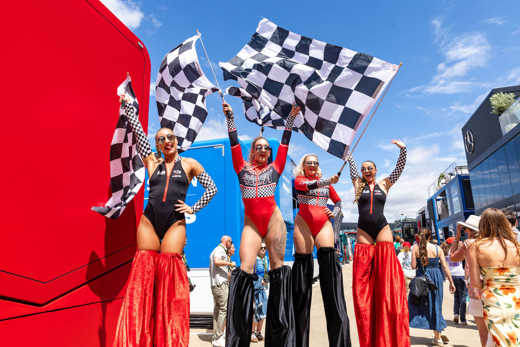 Women on stilts waving chequered flags in the paddock during the 2026 British Grand Prix, photographed by London event photographer Harvey Aspell  