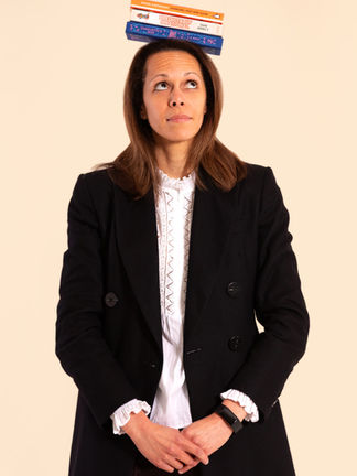 Professional headshot of a woman balancing a stack of books on her head, against a beige background, photographed by London headshot photographer Harvey Aspell