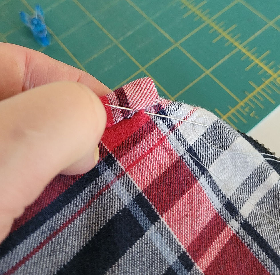 Hand stitching the binding in place to cover the raw seam edges inside a handmade quilted denim pouch.