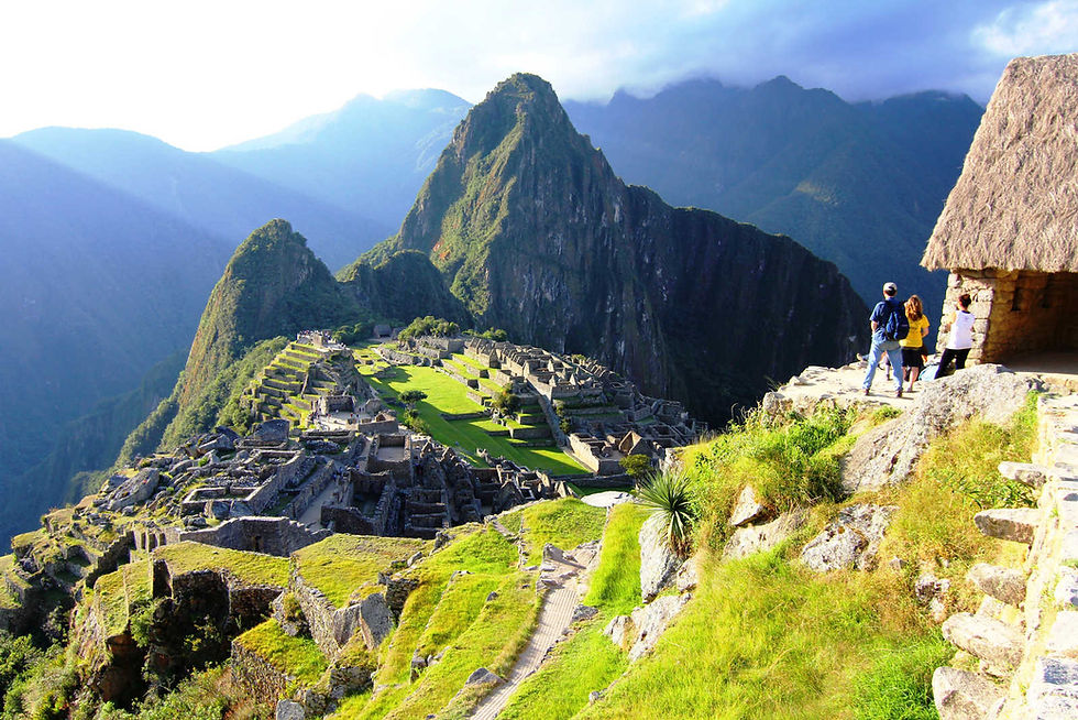Tourists admire Machu Picchu's ancient ruins under a sunny sky, surrounded by lush green terraces and towering mountains.