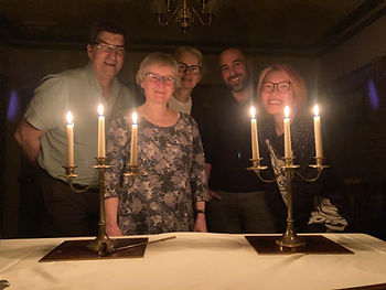 Group of writers standing behind a table on which there are two candelabra with lighted candles. The writers are illuminated by the candlelight.
