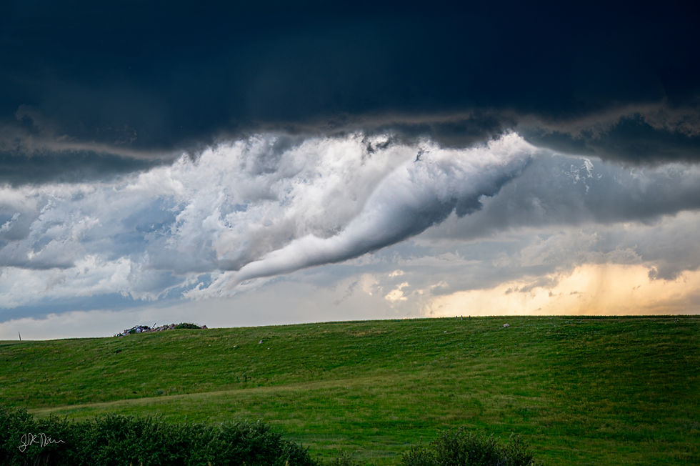An elephant's trunk tornado descends from a dark storm cloud toward a green rolling hill under a dramatic, high-contrast sky.