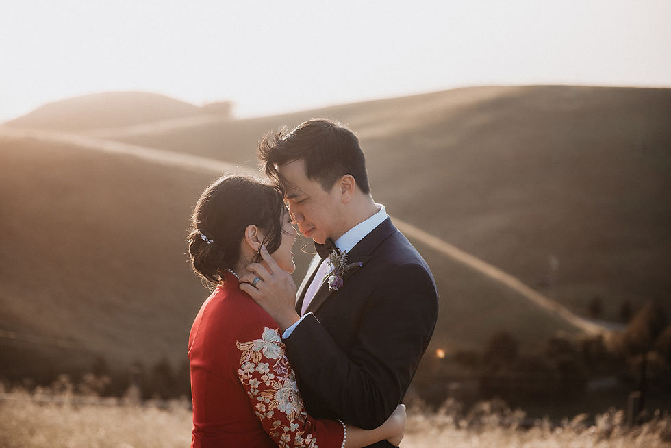 An asian couple holding each other on a sunny hillside on their wedding day. The bride is wearing a traditional red Chinese dress