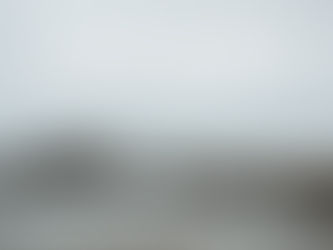 A couple walks hand in hand on a stone jetty by the ocean. Birds fly above, rocks and a sailboat visible in the misty background. Tranquil scene.