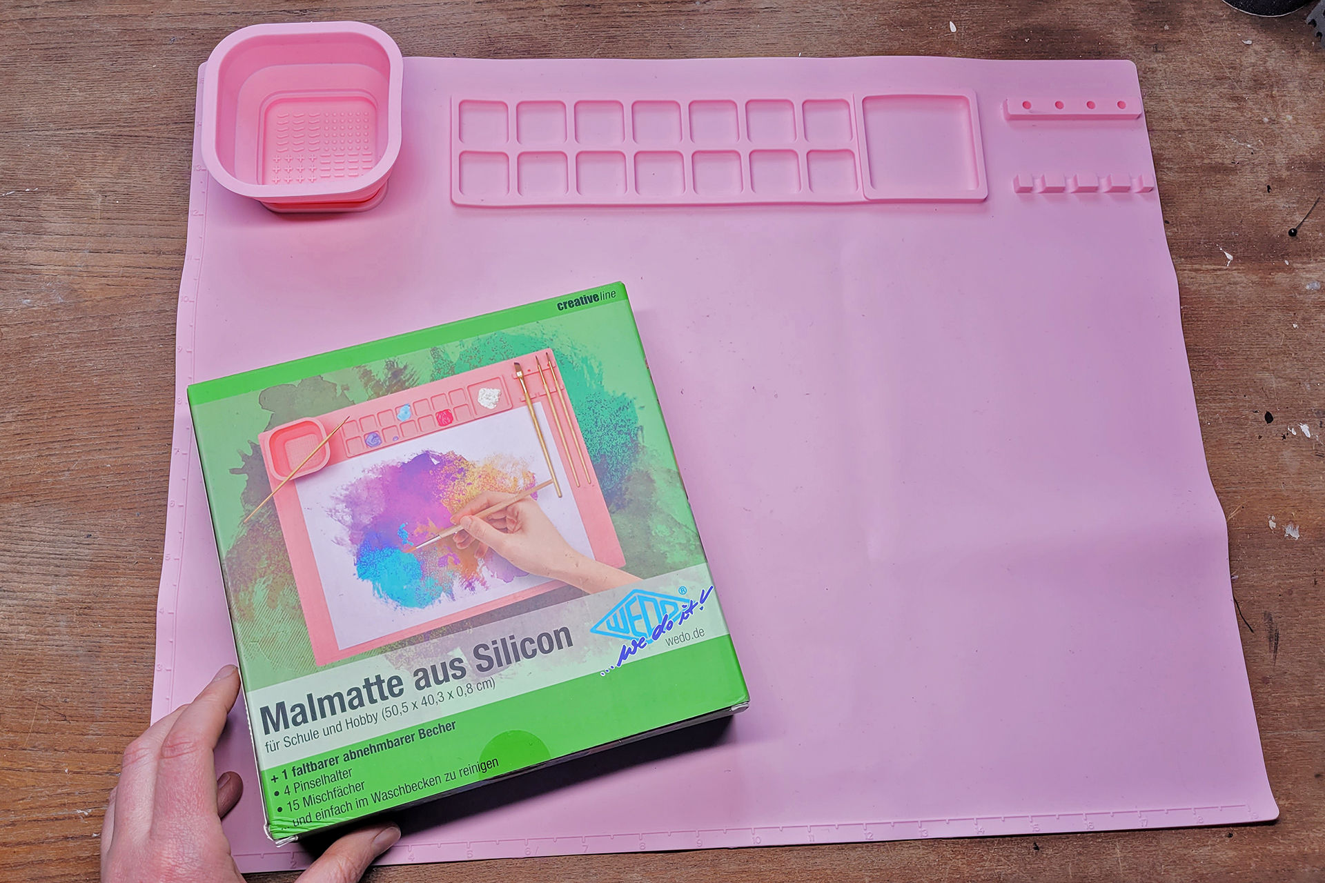 Eine große rosafarbene Silikonmatte mit Fächern zum Farben mischen, Pinselhaltern und einem Wasserbecher
