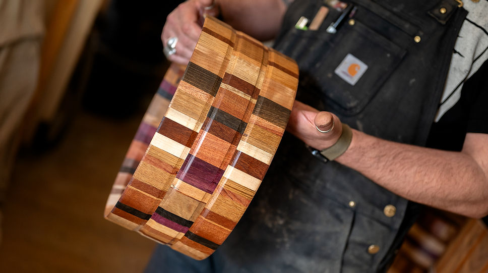Close up of a multi-species stave drum shell - without furniture, held and being checked over by its maker - the founder of Bersoni Custom Drums. It's a colour image and landscape in orientation. The drum shell also has two grooves creating a banded effect around the shell.