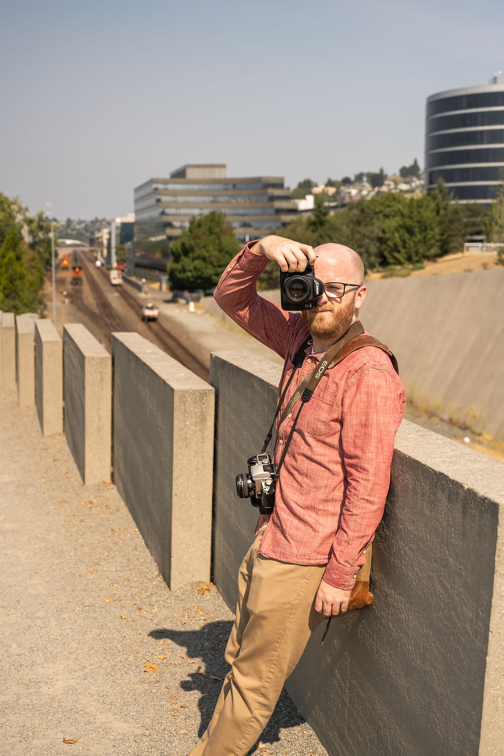 Man taking a photo on an urban walkway overlooking tracks