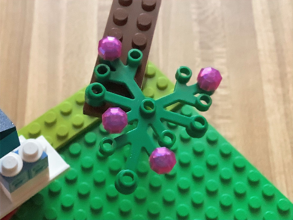 A LEGO tree branch hanging over a LEGO green platform and LEGO snack stand with pink gem flowers and green leaves in the build Playground Garden on the website createsparkle.