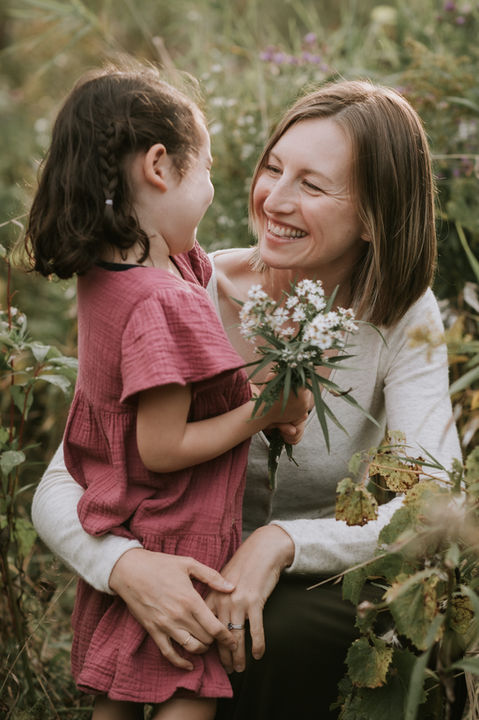 Young mother with daughter in glowing field of wildflowers.