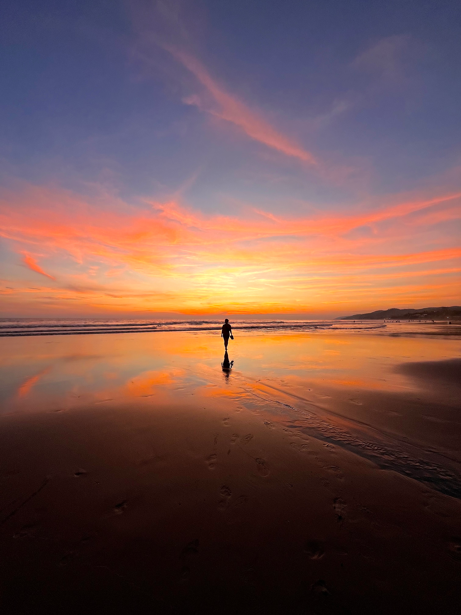 A woman walking on a beach when sun is setting behind her-