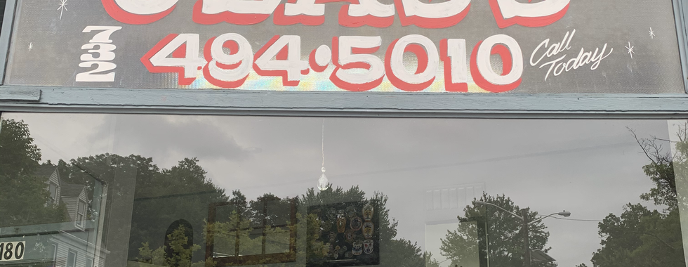 Storefront window of a glass shop in New Jersey featuring a custom hand-painted sign with bold red lettering and the phone number ‘494-5010.’