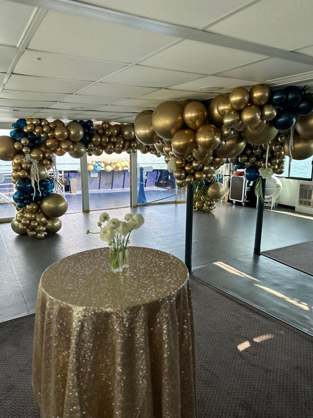 Gold and navy balloon garland framing an entrance, with a gold sequinned cocktail table in front