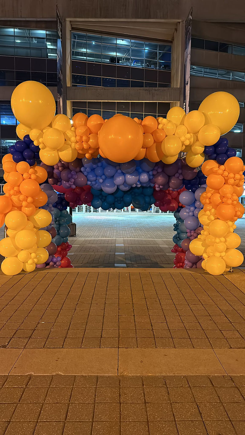 An orange, gold and navy balloon arch over an indoor walkway