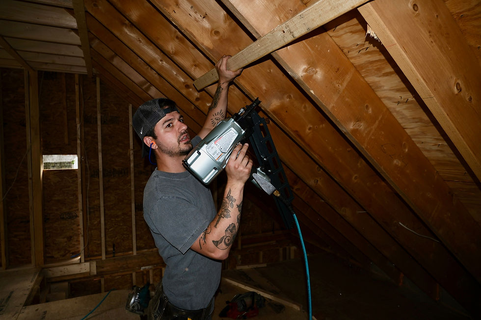 Carpenter using a nail gun on wooden attic rafters.