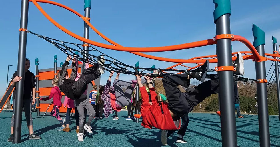 Kids play on a colorful jungle gym under a clear sky, hanging and climbing energetically. The ground is blue, enhancing the playful mood.