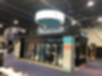A professionally designed trade show booth setup with branded displays, lighting, and interactive elements at a convention center.