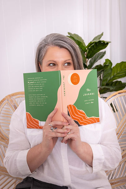 A woman/counsellor cheekily covering her face, accept her eyes, holding a journal in her hands, looking to the left of her.