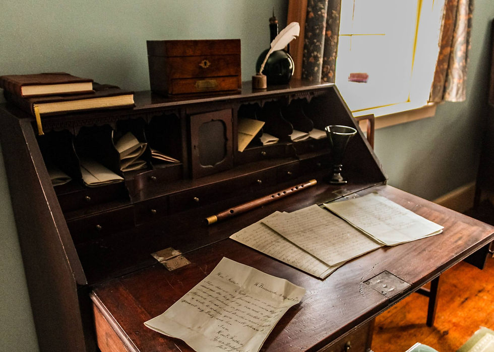 On an old desk at Commissariat House are old letters, a feather pen, and old books.