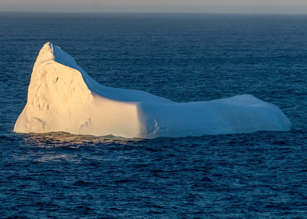 The setting sun casts an illuminating glow on the tall end of this wedge-shaped iceberg in the ocean near the Pouch Cove coast.