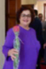 Smiling woman in purple holding a single wrapped red rose.