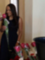 Woman in black dress smiling and holding a long-stemmed red rose.